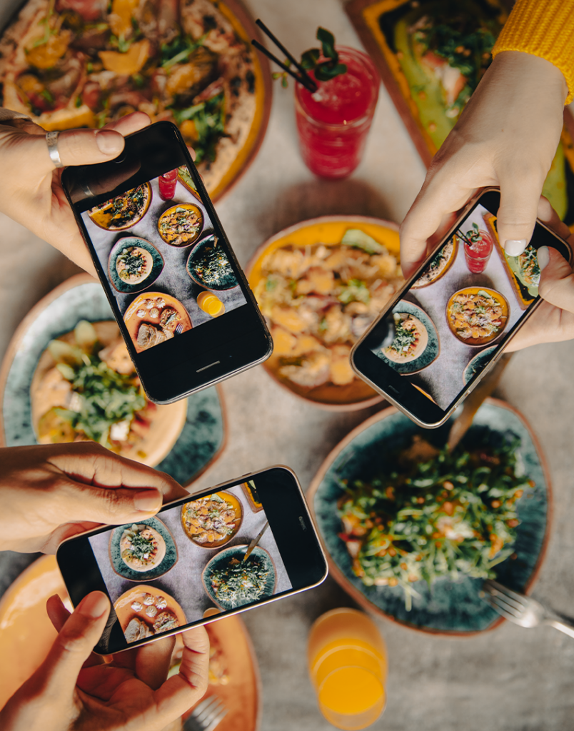 an image of people at a restaurant table taking photos, showcasing one of the ways to create user generate content for restaurants to leverage on social media.